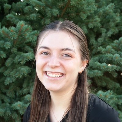 Case Manager Breanna Smiling Outdoors In Front Of Pine Tree